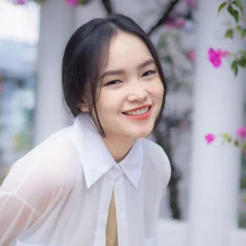 Cheerful young woman in a white blouse smiling in a vibrant garden setting in Ho Chi Minh City.