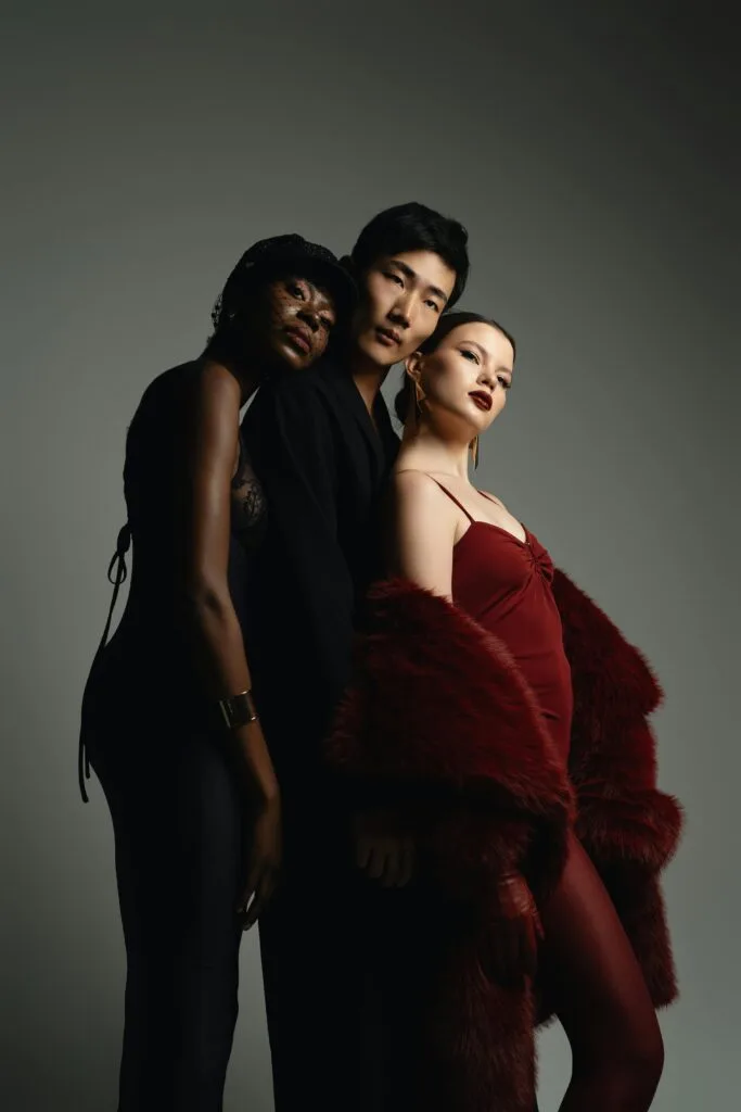 Three models pose elegantly in a studio, showcasing diverse fashion styles and moody lighting.