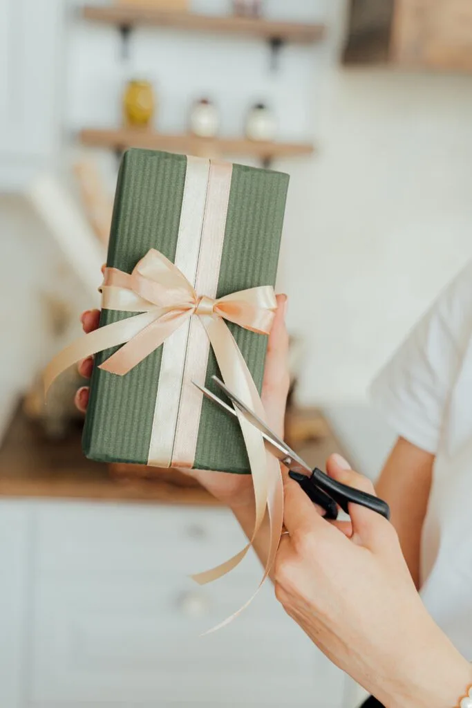 Hands wrapping a green gift box with a satin ribbon. Perfect for celebrations and seasonal gift-giving.