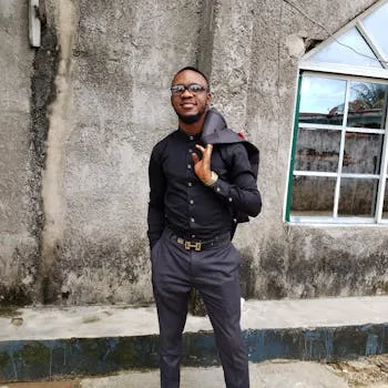 A stylish man in black clothing poses confidently against a concrete wall in Calabar, Nigeria.